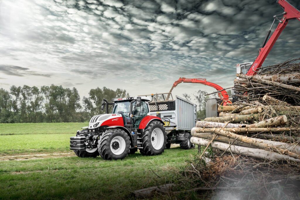 STEYR 6175 Impuls CVT traktor i arbeid med tømmerlasting på et skogsområde.