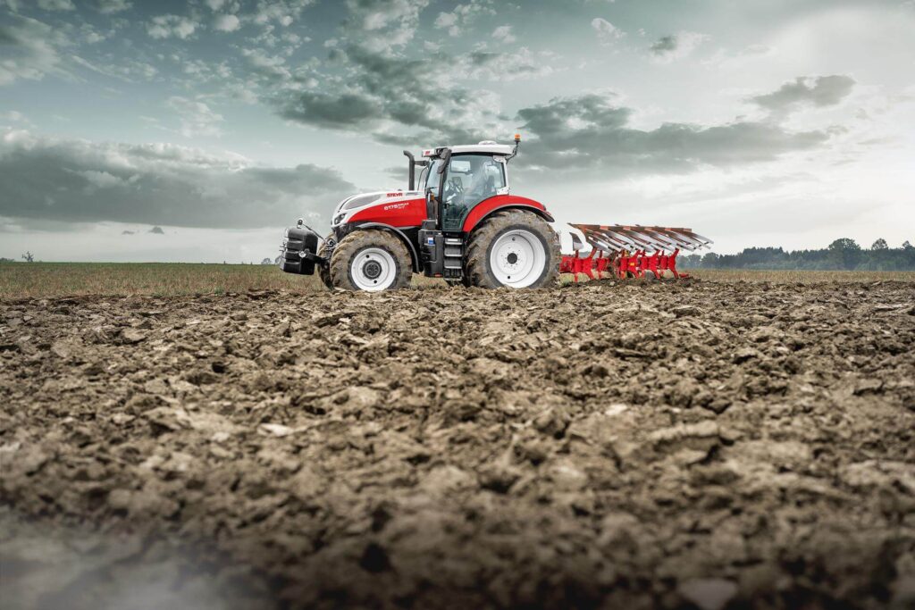 STEYR 6175 Impuls CVT traktor med plog i aksjon på et jordet område.