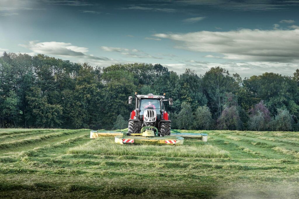 STEYR 6175 Impuls CVT traktor sett ovenfra forfra med Krone slåmaskin i aksjon på en eng.