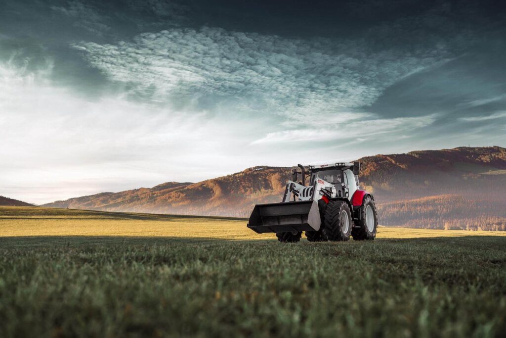 STEYR 6175 Impuls CVT traktor med frontlaster, avbildet mot et vakkert landskap.