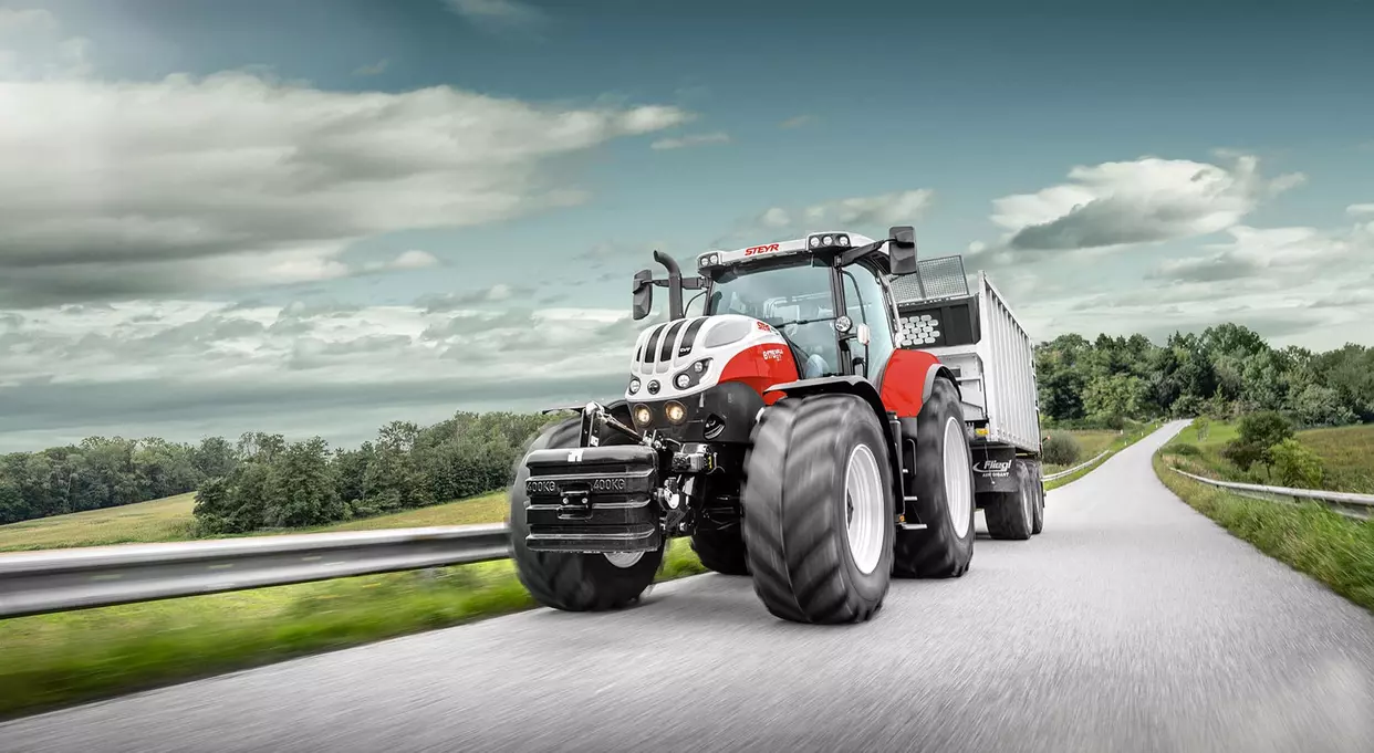 Steyr Impuls CVT-traktor kjørende på vei med en Fliegl tilhenger festet bak.