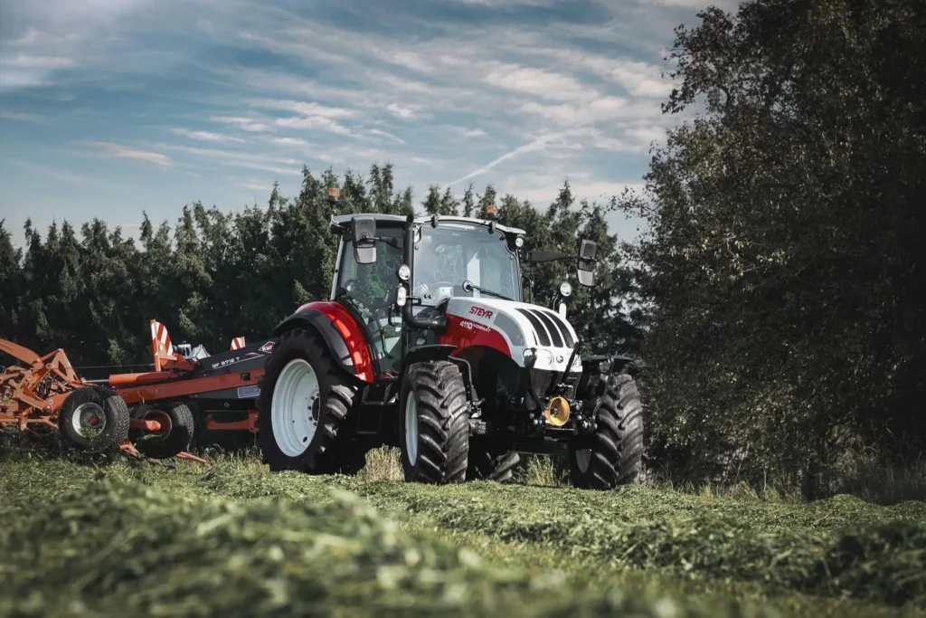 En STEYR 4110 Kompakt traktor jobber med en slåmaskin i et grønt jorde.