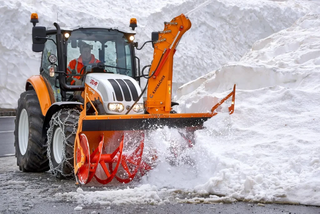 En oransje STEYR 4105 traktor med frontmontert snøfres.