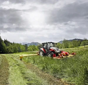 En allsidig og kompakt Steyr-traktor står på en grønn eng omgitt av trær og åser i bakgrunnen, perfekt for mindre gårder og presisjonsarbeid.