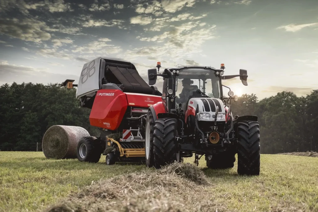 STEYR traktor med rundballepresse fra Pöttinger i aksjon på en eng.