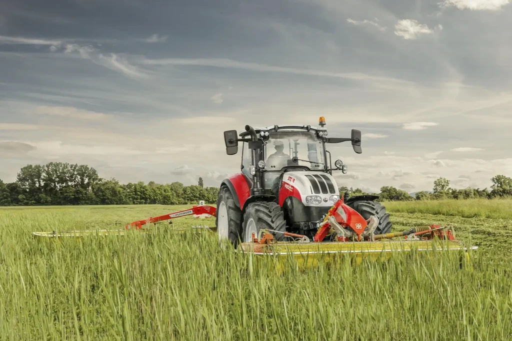 Steyr 4120 Multi-traktor med Krone slåmaskiner som klipper gress på et jorde.