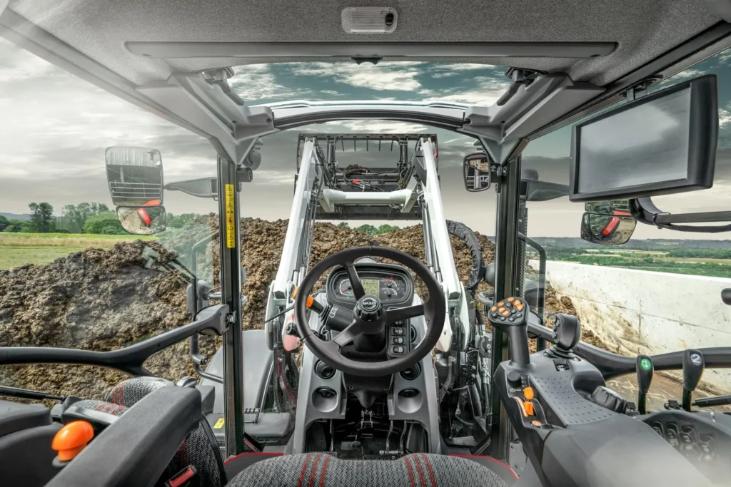 Utsikt fra førerhytten på en STEYR traktor med frontlaster som håndterer gjødsel.