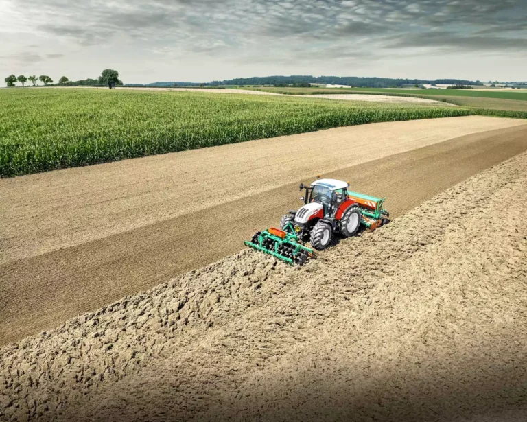 En Steyr Multi-traktor pløyer markene i et stort jordbrukslandskap med kornåkre i bakgrunnen, som demonstrerer sin kraft og allsidighet.