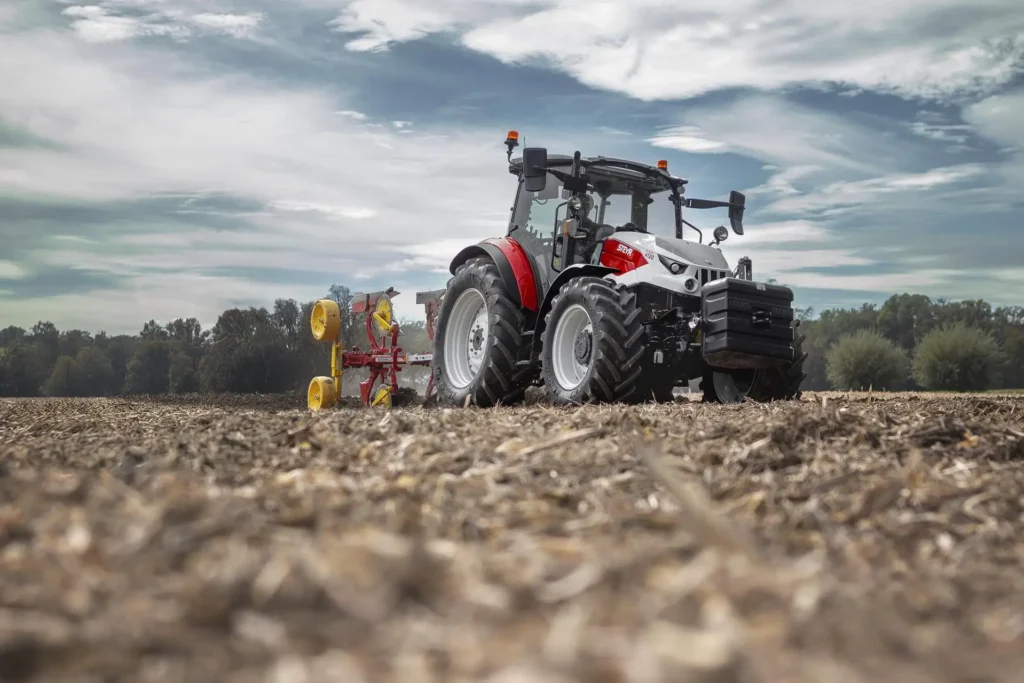 Lav vinkel av Steyr Plus-traktor med plog, sett fra bakkenivå på et jorde.