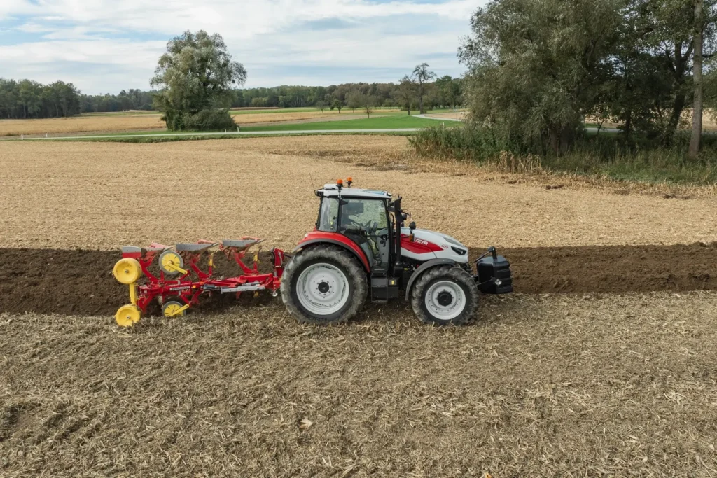 Steyr Plus-traktor med plog i arbeid på en åker, som lager jevne plogfurer.