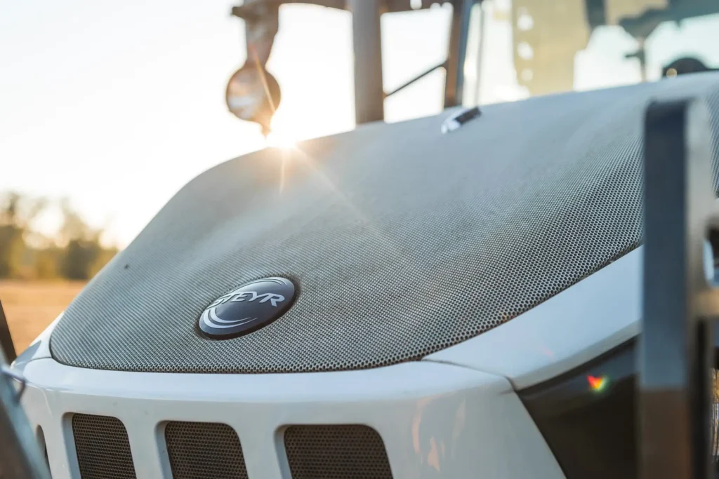 Nærbilde av Steyr Plus-traktorens frontgrill med Steyr-logoen i solnedgang.