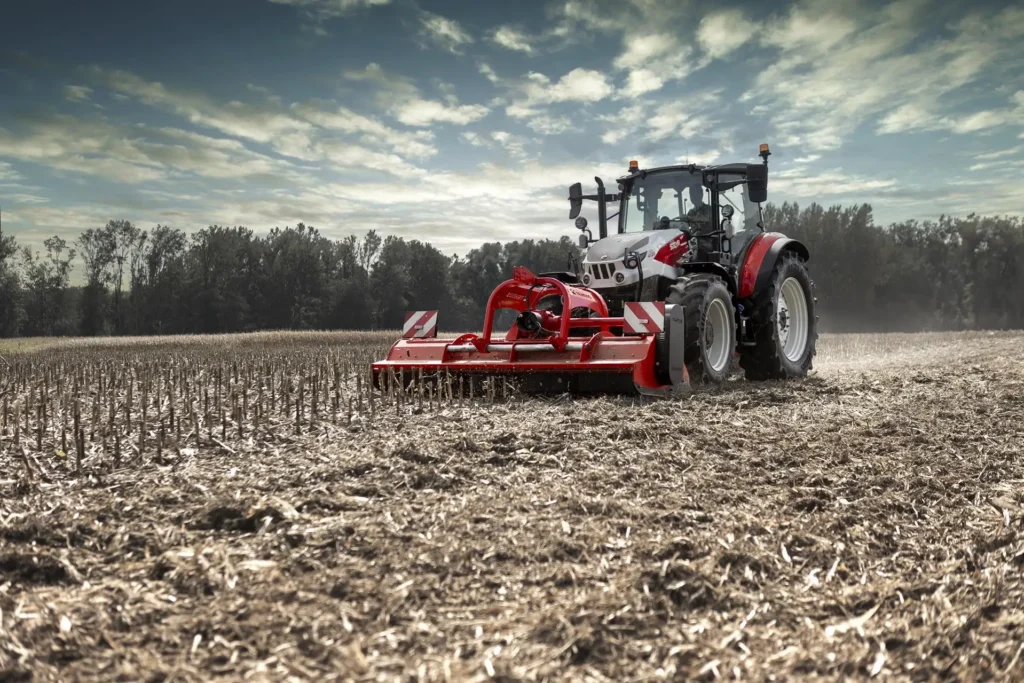 Steyr Plus-traktor i profil med jordbruksutstyr, klar til å starte en ny arbeidsdag på åkeren.