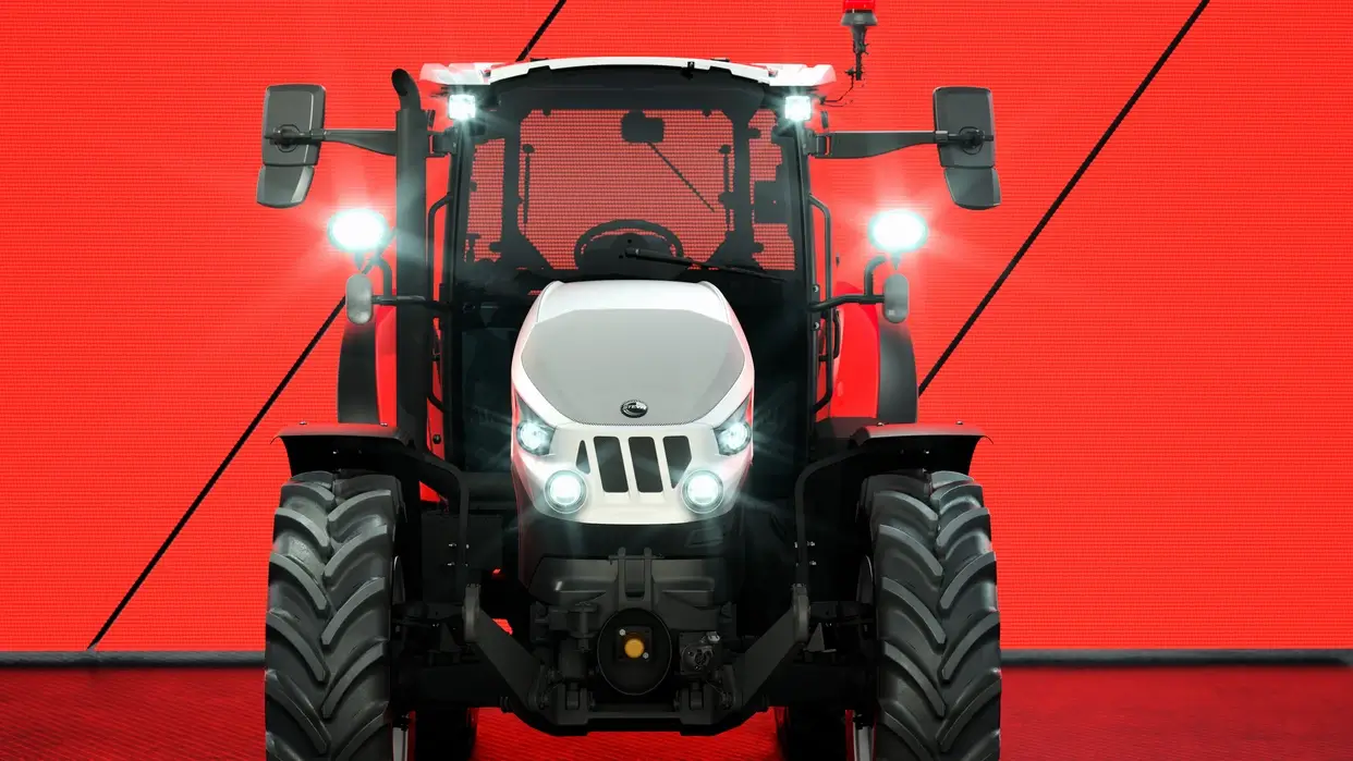 Frontbilde av en Steyr-traktor med LED-lys påslått, stående foran en lysende rød bakgrunn, fremhever det moderne designet og kraftige fronten.