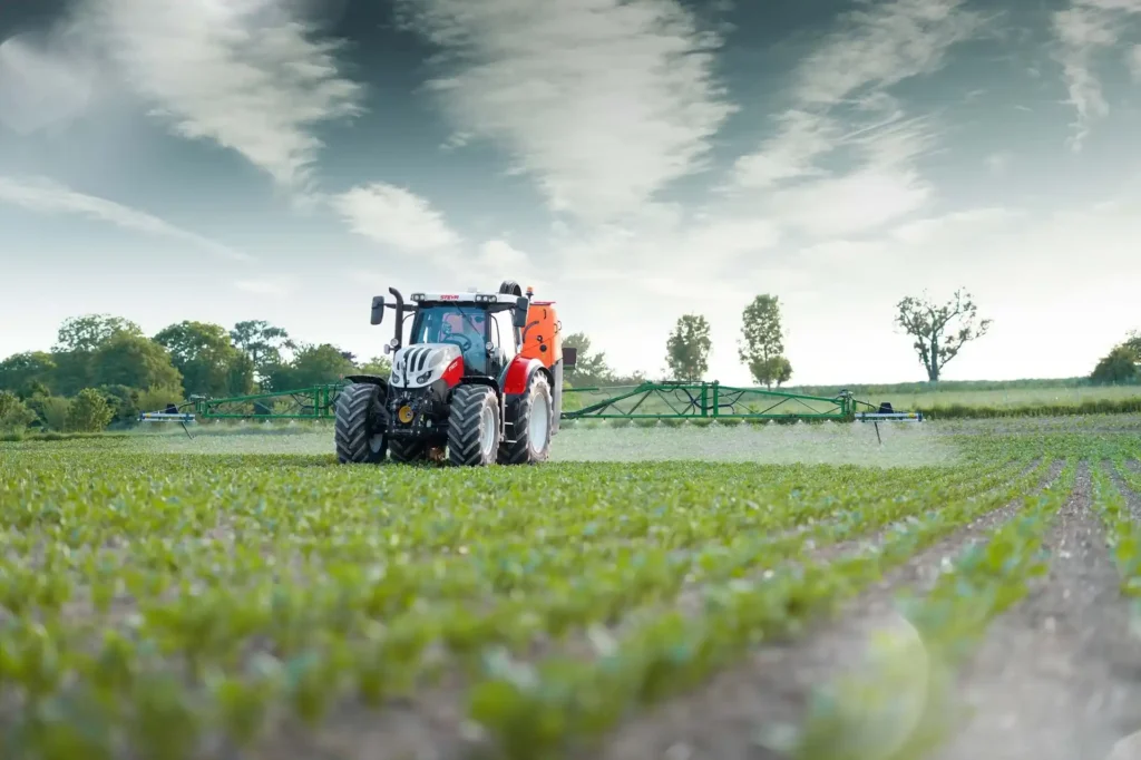 Steyr Profi traktor sprøyter åkeren med plantevernmiddel, med grønne avlinger i forgrunnen.