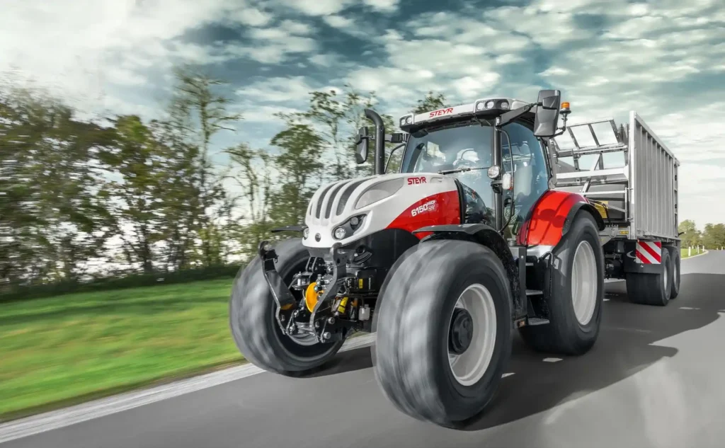 Steyr Profi traktor med henger, kjører på vei i høy hastighet med en dynamisk bevegelseseffekt.