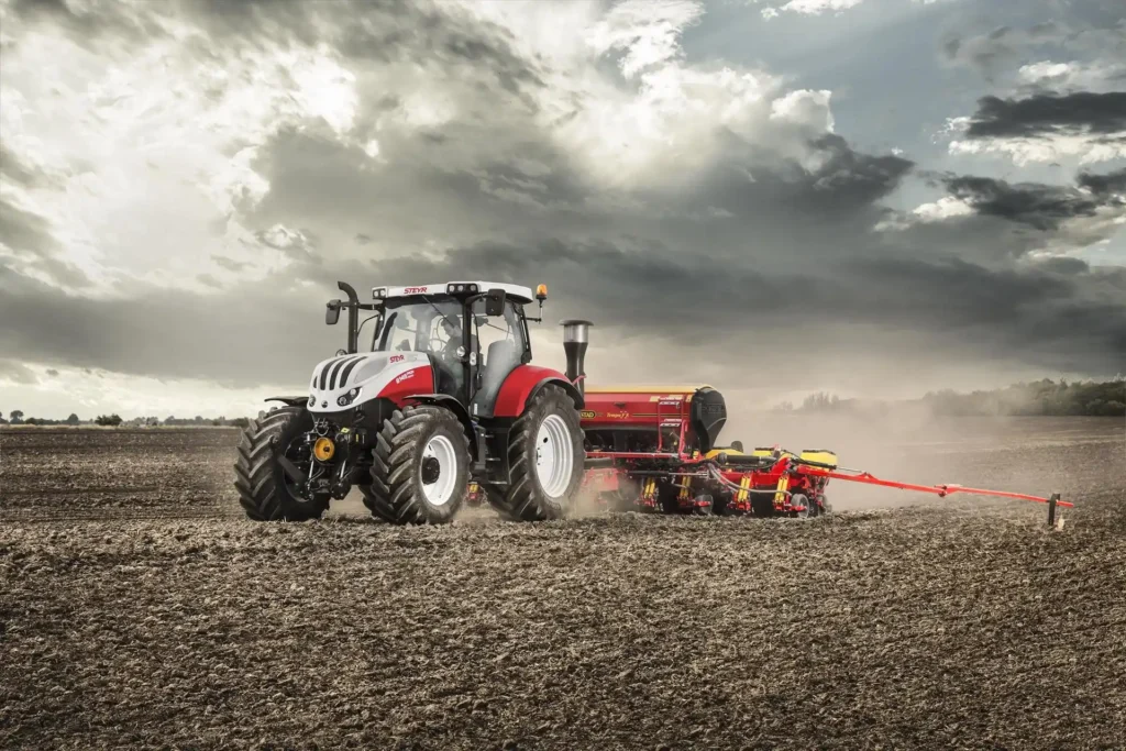 Steyr Profi traktor trekker en plog over en åker, dramatisk vær og åslandskap i bakgrunnen.