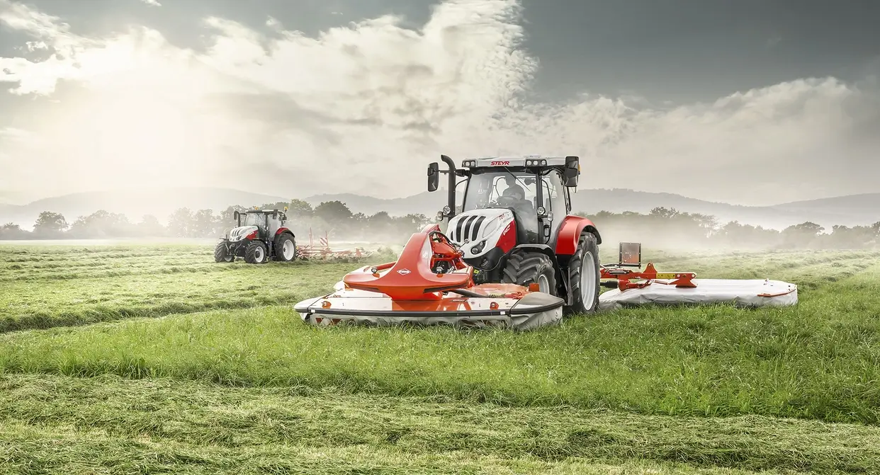 En Steyr Profi 6145 traktor med en slåmaskinkombinasjon på en eng under gresshøsting.