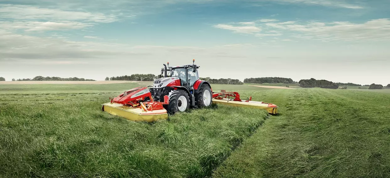 Steyr 6280 Absolut CVT jobber med slåmaskin på et stort jorde under blå himmel.