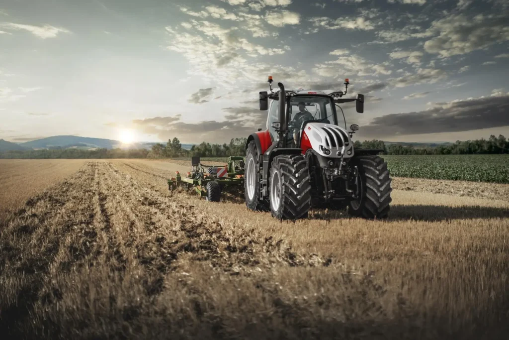 Steyr Terrus 6300 traktor med kraftige dekk arbeider på et jorde under solnedgang.