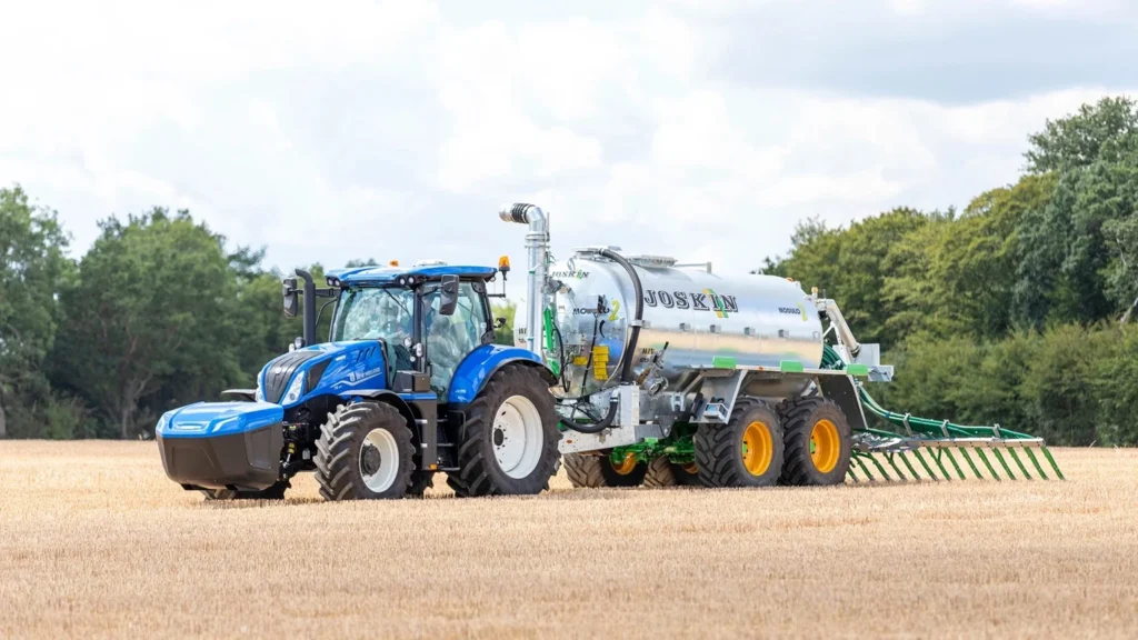 New Holland T6 Methane Power traktor i et åpent jorde, koblet til en Joskin gjødselspreder, som viser effektivitet og bærekraft i landbruksdrift.