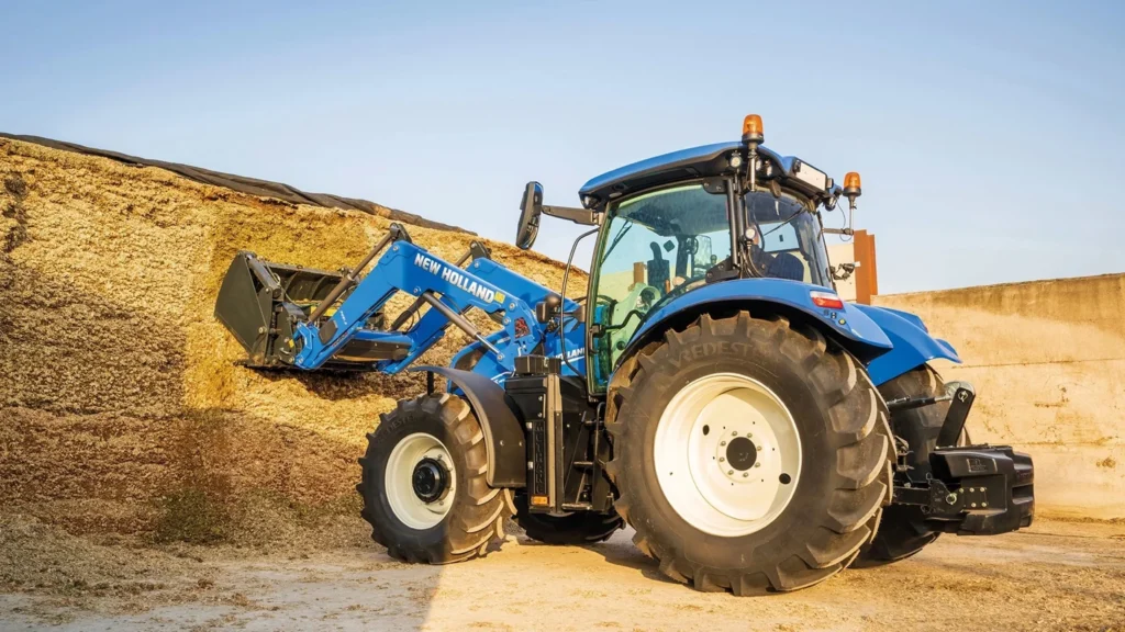 En New Holland T6 Methane Power traktor utstyrt med en frontlaster, som håndterer fôr eller annet materiale, demonstrerer allsidighet og ytelse.