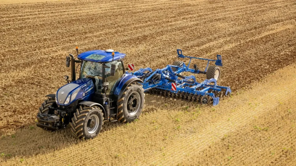 En blå New Holland T7 LWB-traktor som trekker en Joskin-tankvogn over en åker, demonstrerer kraft og kapasitet i landbrukstransport.