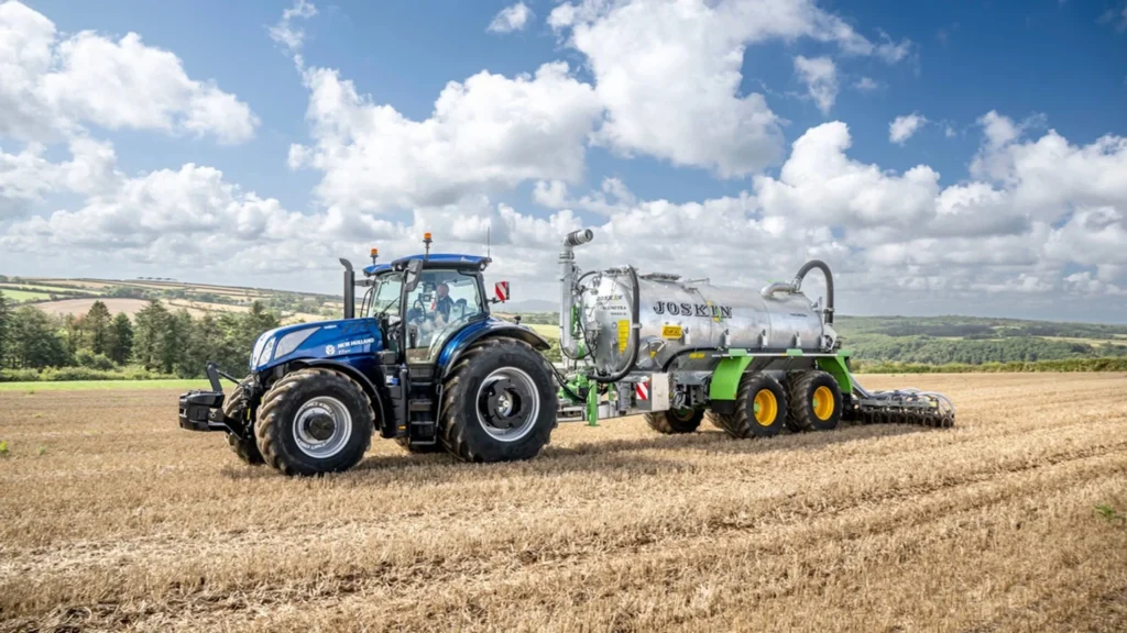 En New Holland T7 LWB-traktor som driver jordbearbeiding med et blått redskap på en åker, viser presisjon og ytelse.