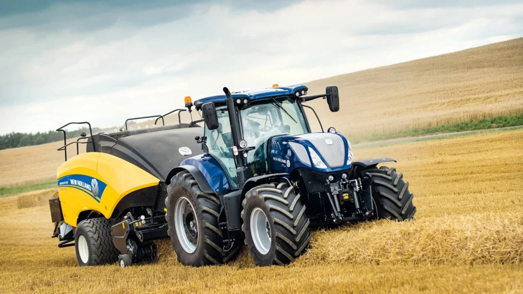 New Holland-traktor med ballepresser på en gyllen kornåker.