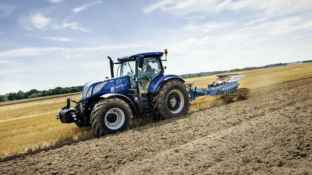 New Holland-traktor med plog som pløyer en åker på en klar dag.