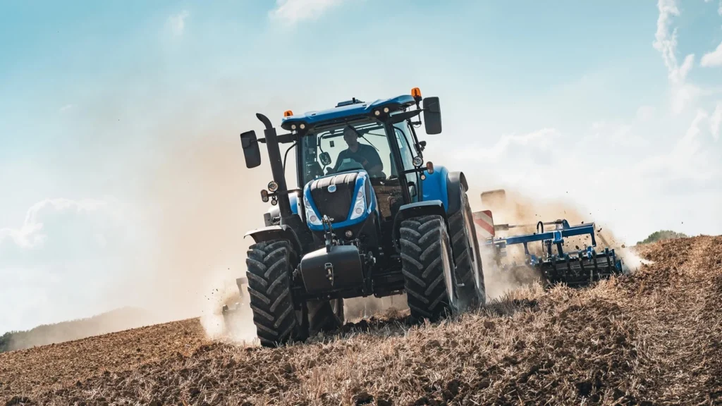 New Holland T/ SWB som arbeider på en åker, skaper støvsky under pløying.