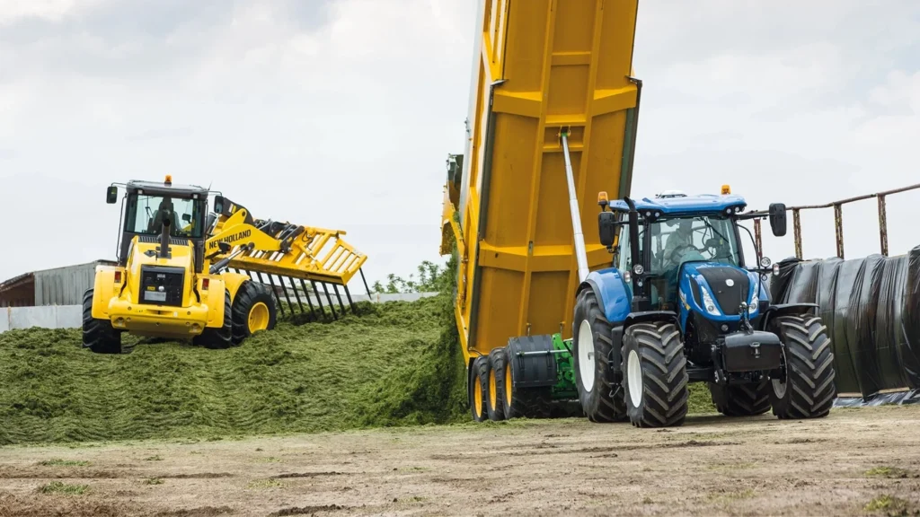 Traktor og laster som flytter grønn masse på en gårdsplass.