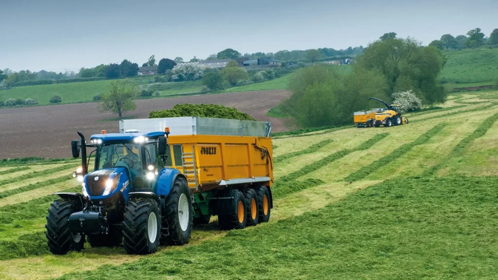 New Holland-traktor med gult tilhengerlass, omgitt av grønne enger.