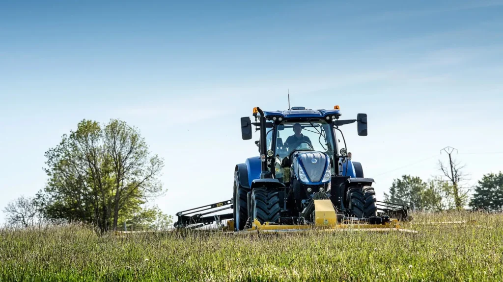 New Holland-traktor sett forfra i en grønn eng med trær i bakgrunnen.