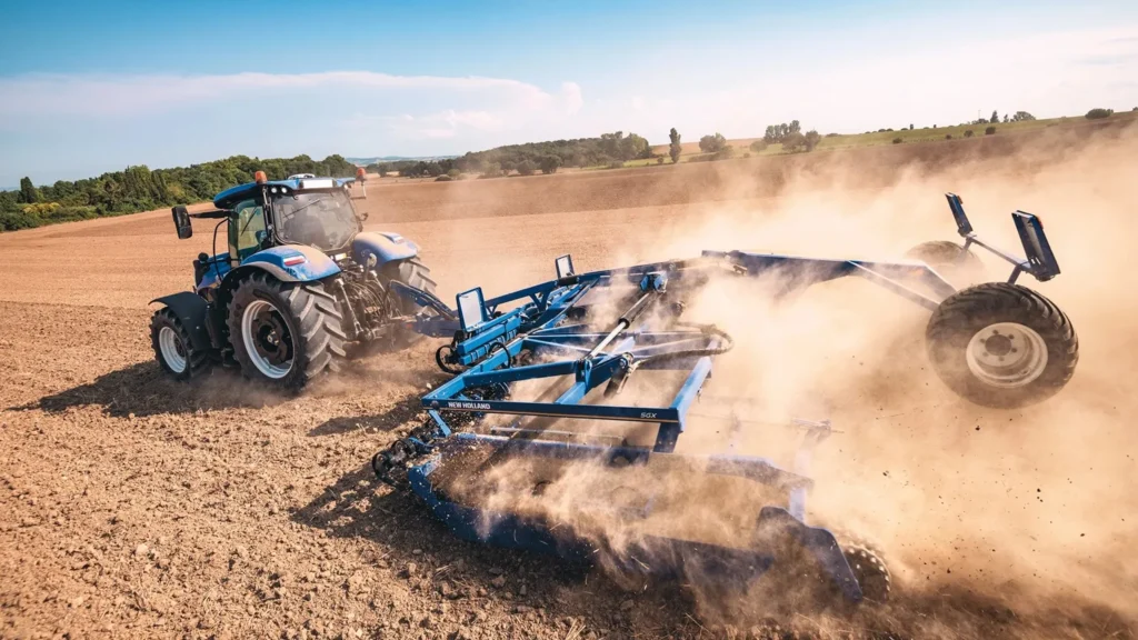 New Holland-traktor med jordbruksutstyr som lager støv på en åker.